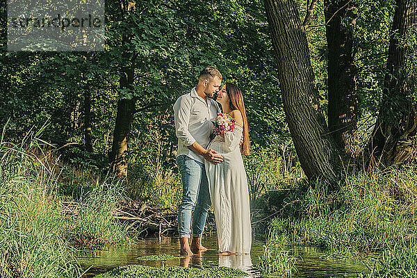 Affectionate couple standing on stream near forest