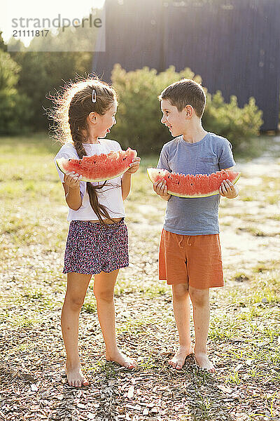 Brother and sister holding watermelon in public park