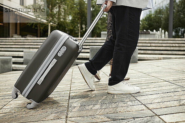 Senior man dragging wheeled suitcase and walking with woman in street