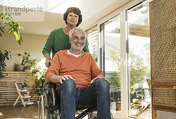 Smiling man on wheelchair assisted by wife at home