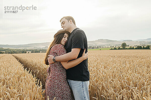 Young affectionate couple standing and embracing in agricultural field