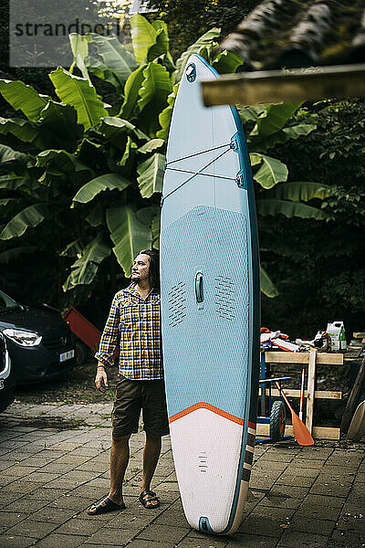 Man standing near surfboard at back yard