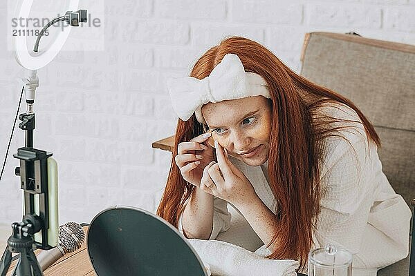 Teenager filming beauty tutorial with makeup in front of a mirror at home.