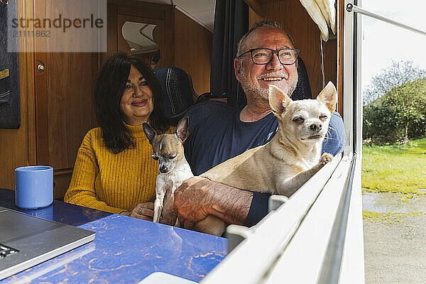 Happy elderly couple with dogs near window of motor home