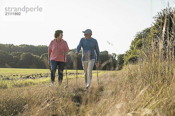 Senior couple with hiking poles walking on meadow