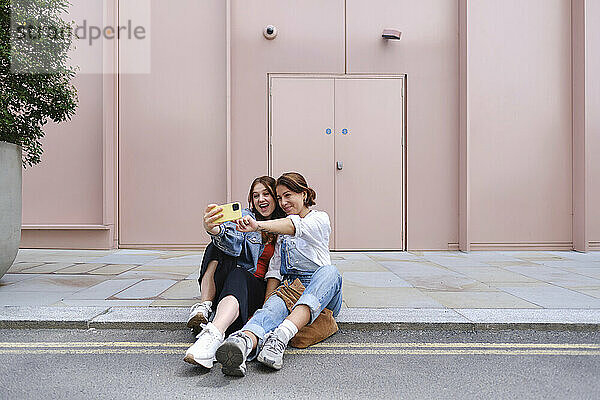 Gay couple sitting and taking selfie on sidewalk