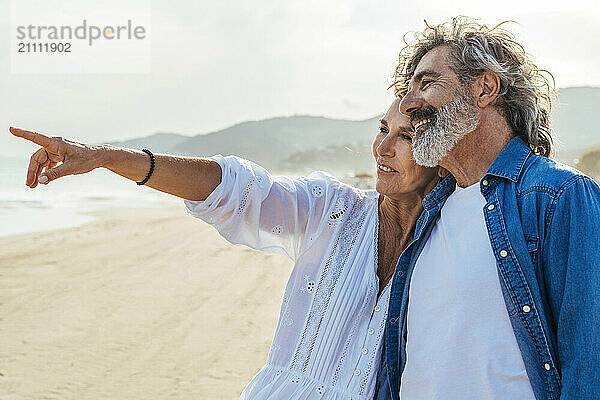 Smiling senior woman gesturing with man standing at beach