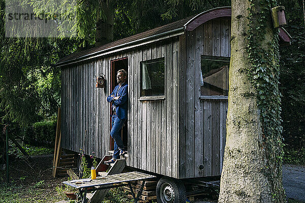 Mature businessman standing at doorway of log cabin