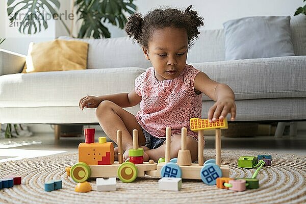 Cute girl playing with toy vehicle on rug at home