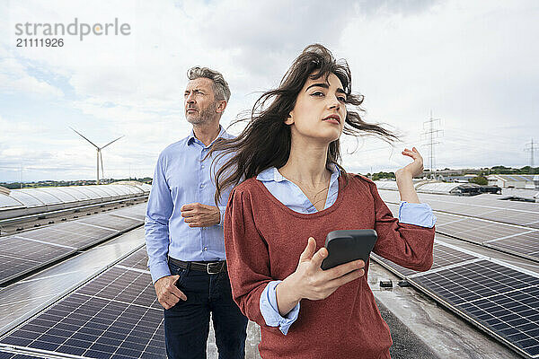 Young colleague holding smart phone with businessman walking on rooftop