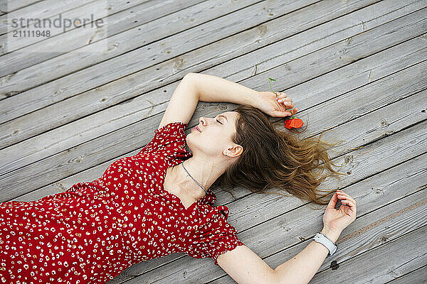 Carefree woman lying down with arms raised on wooden patio