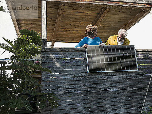 Senior couple holding solar panel at balcony in house