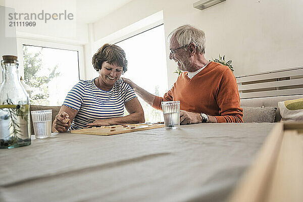 Happy man sitting near table and playing board game with wife at home