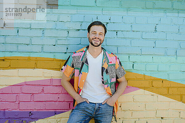 Happy man with hands in pockets standing in front of wall