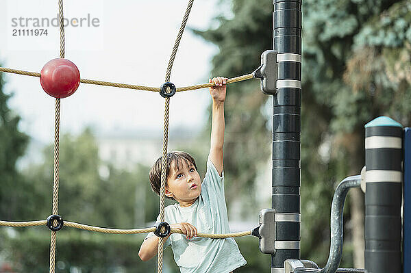 Determined boy climbing on rope at jungle gym