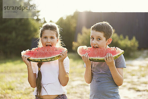 Siblings eating slices of watermelon in public park