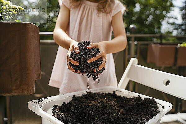 Girl holding soil from tray at balcony