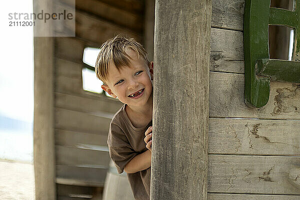 Smiling boy peeking through wooden house