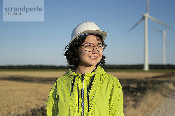 Smiling young engineer wearing reflective jacket at wind farm