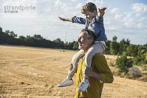 Boy with arms outstretched sitting on grandfather's shoulders