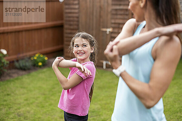 Smiling girl doing stretching exercise with mother in back yard