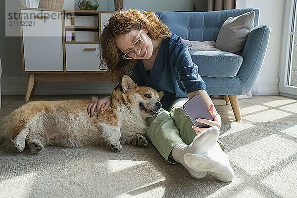 Young woman taking selfie with pet dog on smart phone at home