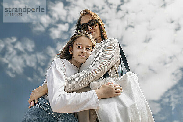 Happy mother embracing daughter under cloudy sky