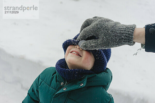 Hand of father pulling knit hat of son over face in winter