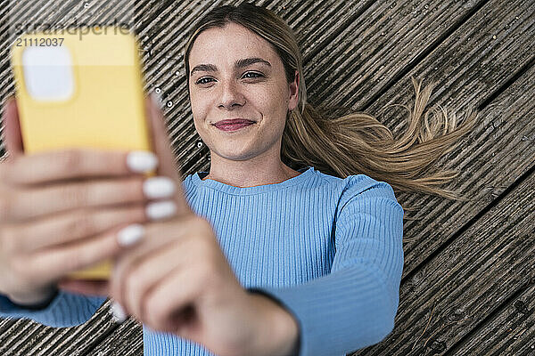 Beautiful young woman using smart phone and lying on wooden patio