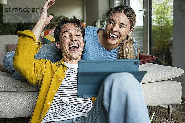 Cheerful young couple having fun using tablet PC at home