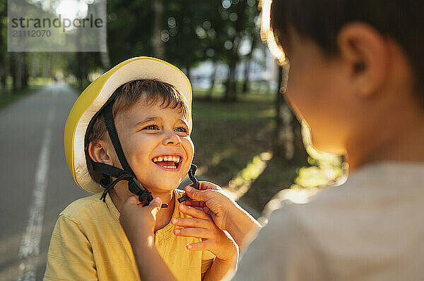 Cheerful boy wearing helmet with help of brother near road