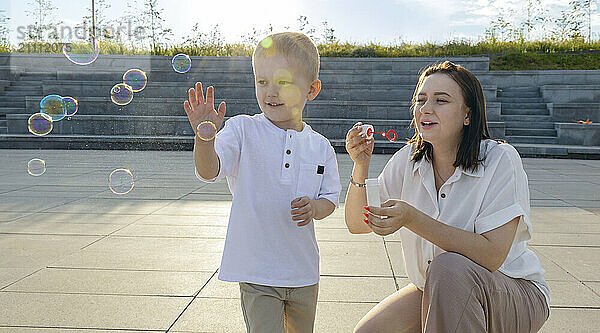 A dark-haired woman blows bubbles with her son.