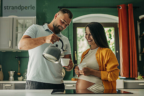 Pregnant woman with husband pouring tea in cup at home