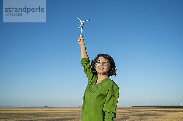 Smiling engineer holding wind turbine model in field