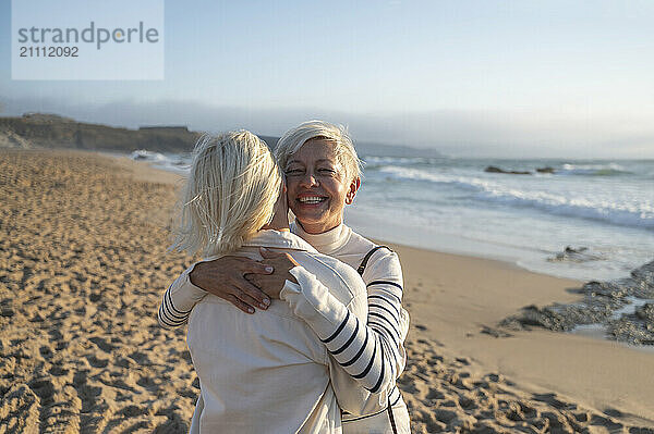 Happy woman embracing daughter at beach on sunny day