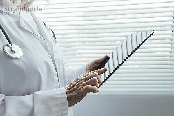 Hands of senior doctor using tablet PC in front of window