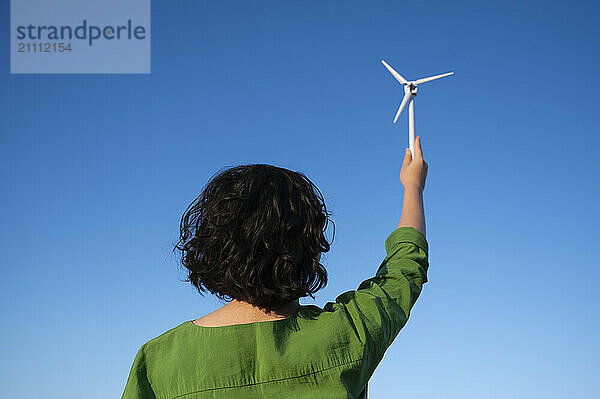 Engineer holding wind turbine model under clear blue sky