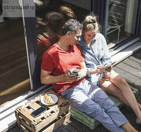 Couple relaxing on balcony with digital tablet