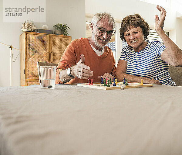 Happy senior couple sitting near table and enjoying board game at home