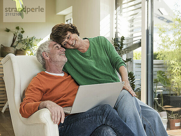 Affectionate couple sitting on chair with laptop at home