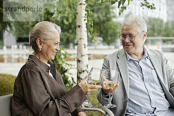 Happy couple toasting with white wine and sitting at outdoor restaurant