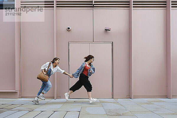 Gay couple holding hands and running in front of building near sidewalk