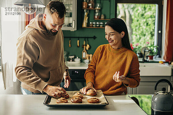 Man with pregnant wife eating cinnamon bun in kitchen at home