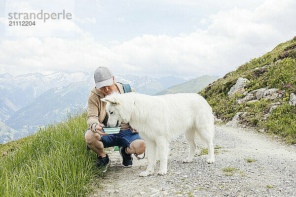 Man feeding drink to dog on dirt road in mountains