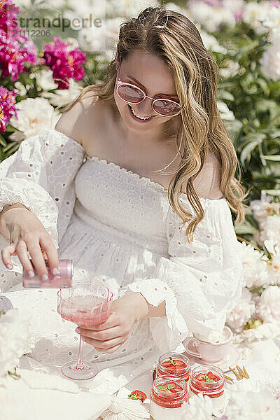 Smiling blond woman wearing sunglasses pouring drink in glass