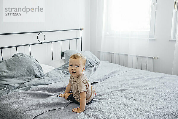 Cute boy sitting on bed at home