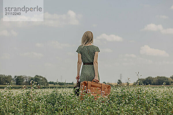 Woman in green dress holding suitcase and standing in field