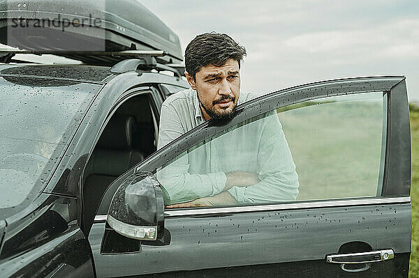 Thoughtful man leaning on car door