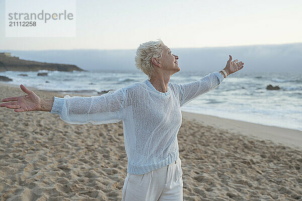 Mature woman with arms outstretched enjoying leisure time at beach