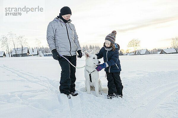 Father and son with sheepdog standing in snow